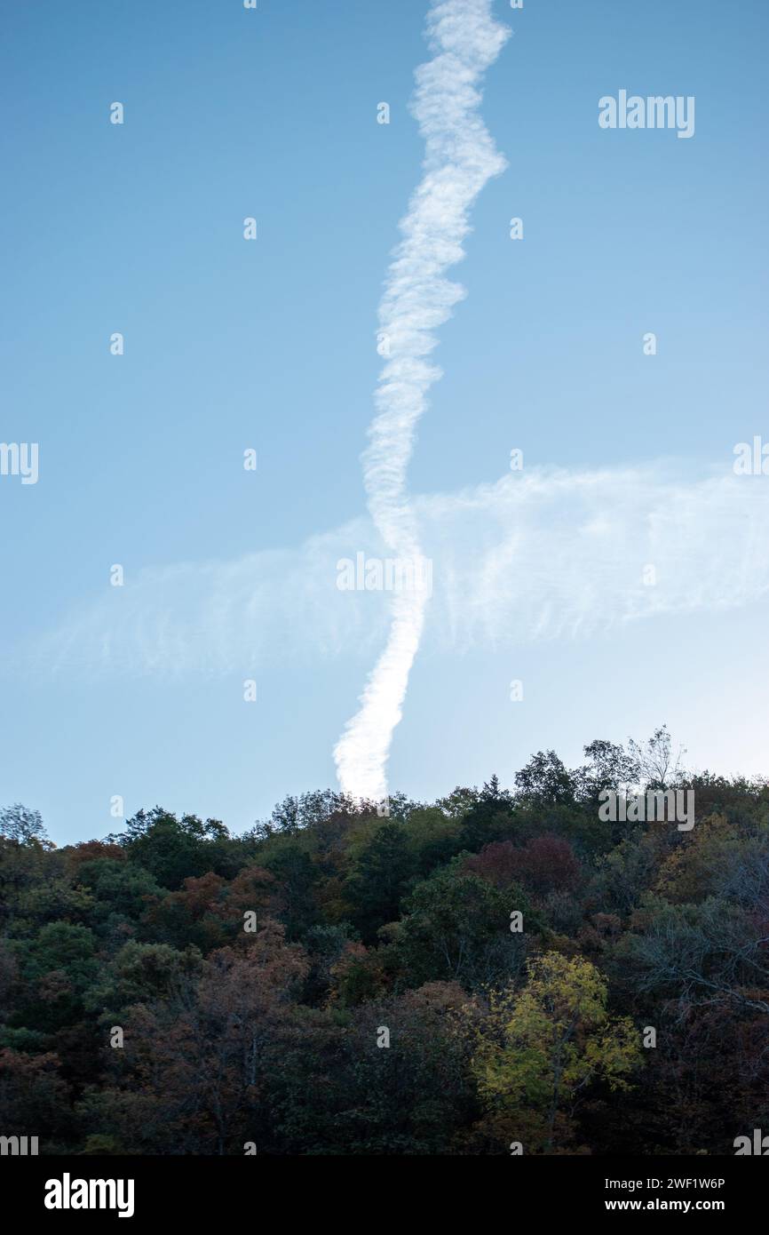 Verticle and horizontal clouds intersect above the tree line in Arkansas creating an unusual display in the blue sky. Bokeh. Stock Photo