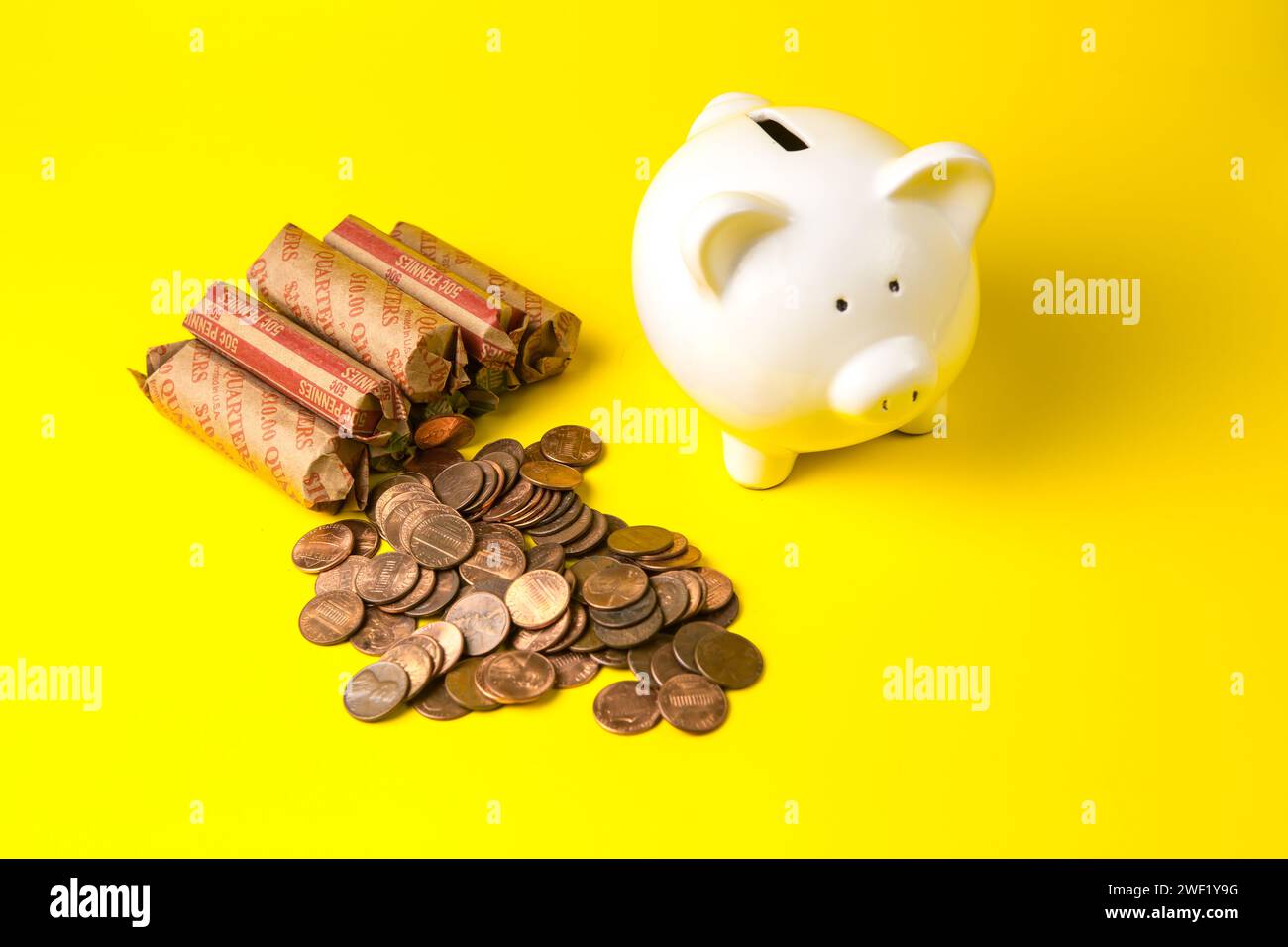 American coin rolls with a white piggy bank on a yellow background Stock Photo