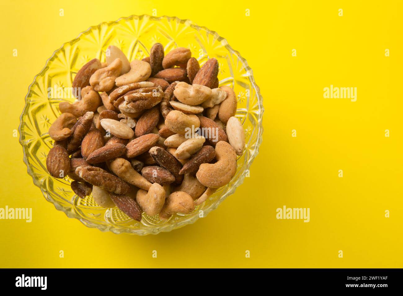 Salted mixed nuts in a glass bowl on a yellow background Stock Photo