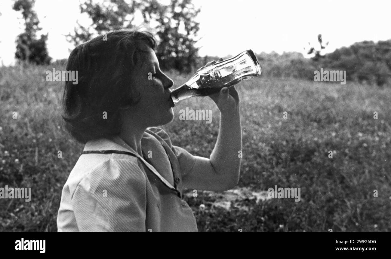 A young girl drinks a glass bottle of Coca Cola, 1950. Stock Photo