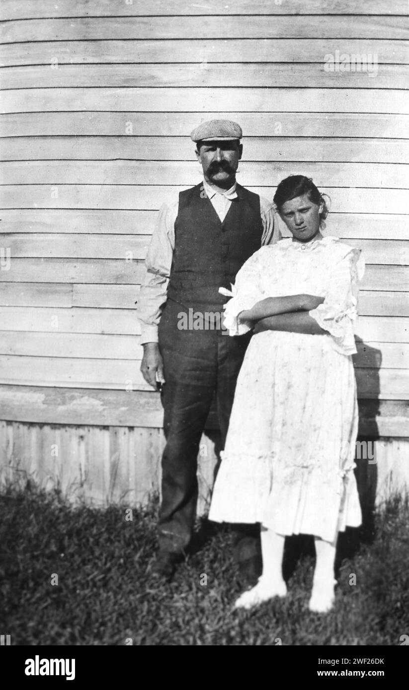 Father and daughter stand against the side of the clapboard house, ca. 1920. Stock Photo
