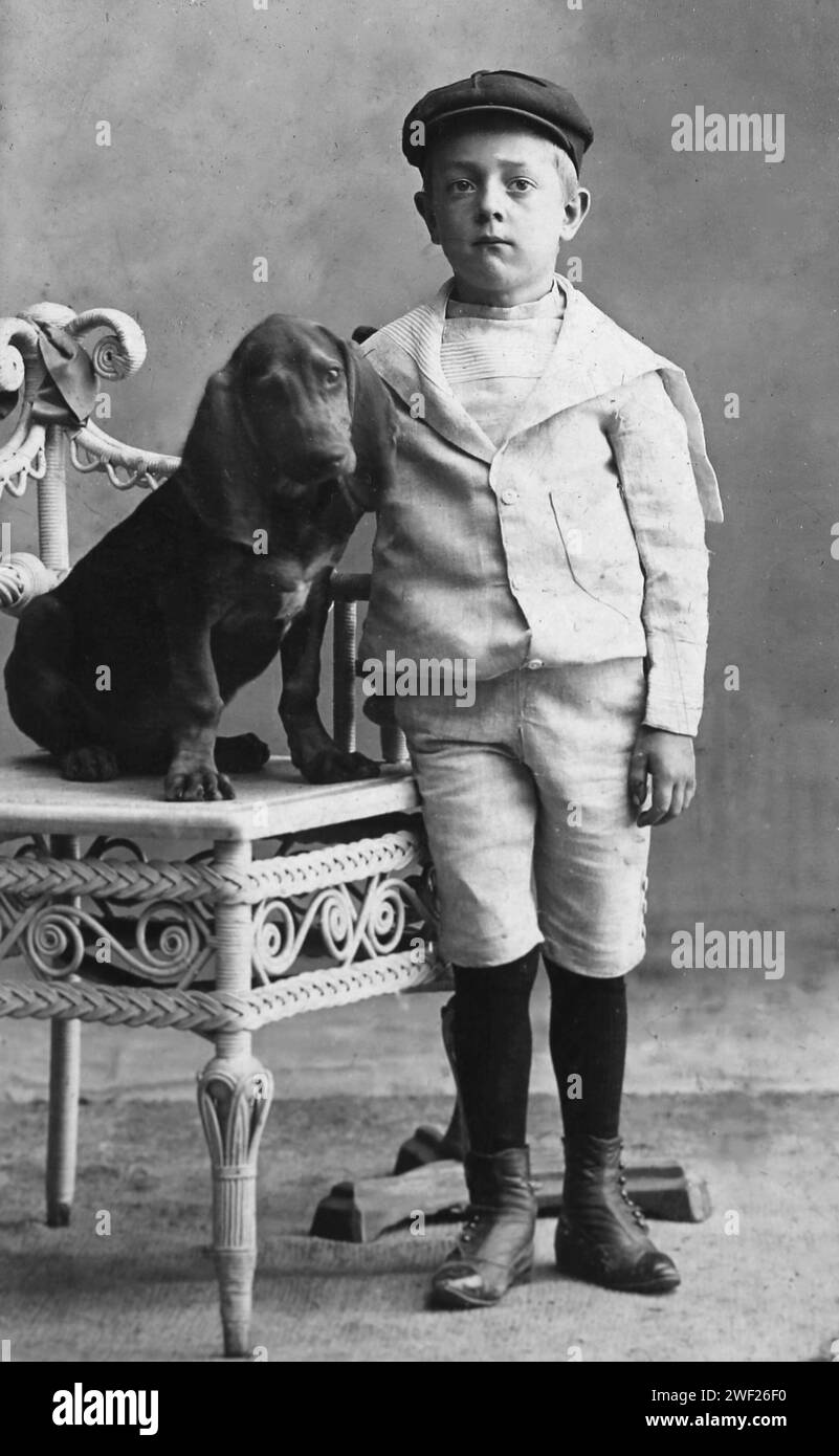 A young boy help held still by a posing stand in back stands for a portrait with his hound dog, ca. 1890. Stock Photo