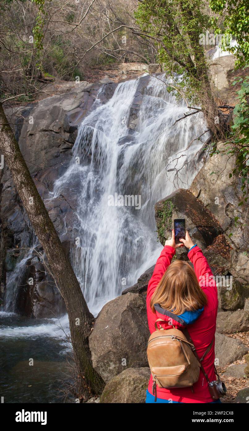 Trekker woman taking pictures with smartphone at Nogaleas waterfall, Jerte Valley, Caceres, Extremadura, Spain Stock Photo