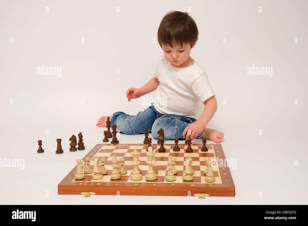 A child is playing chess, studio white background. Baby with chess pieces on a chessboard Stock Photo