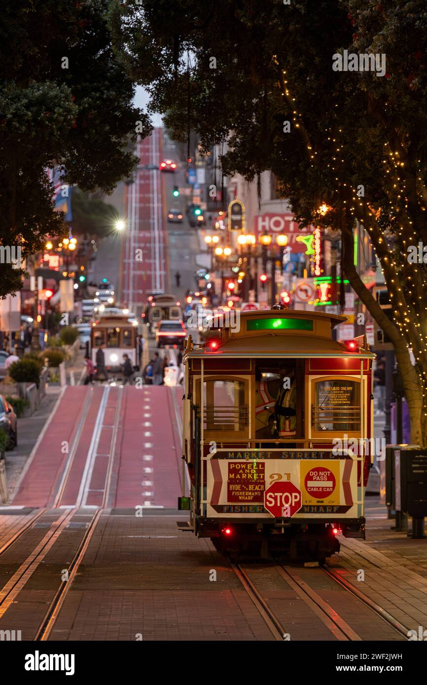 A cable car gracefully descending a bustling city street at night, as pedestrians stroll along the vibrant sidewalk Stock Photo