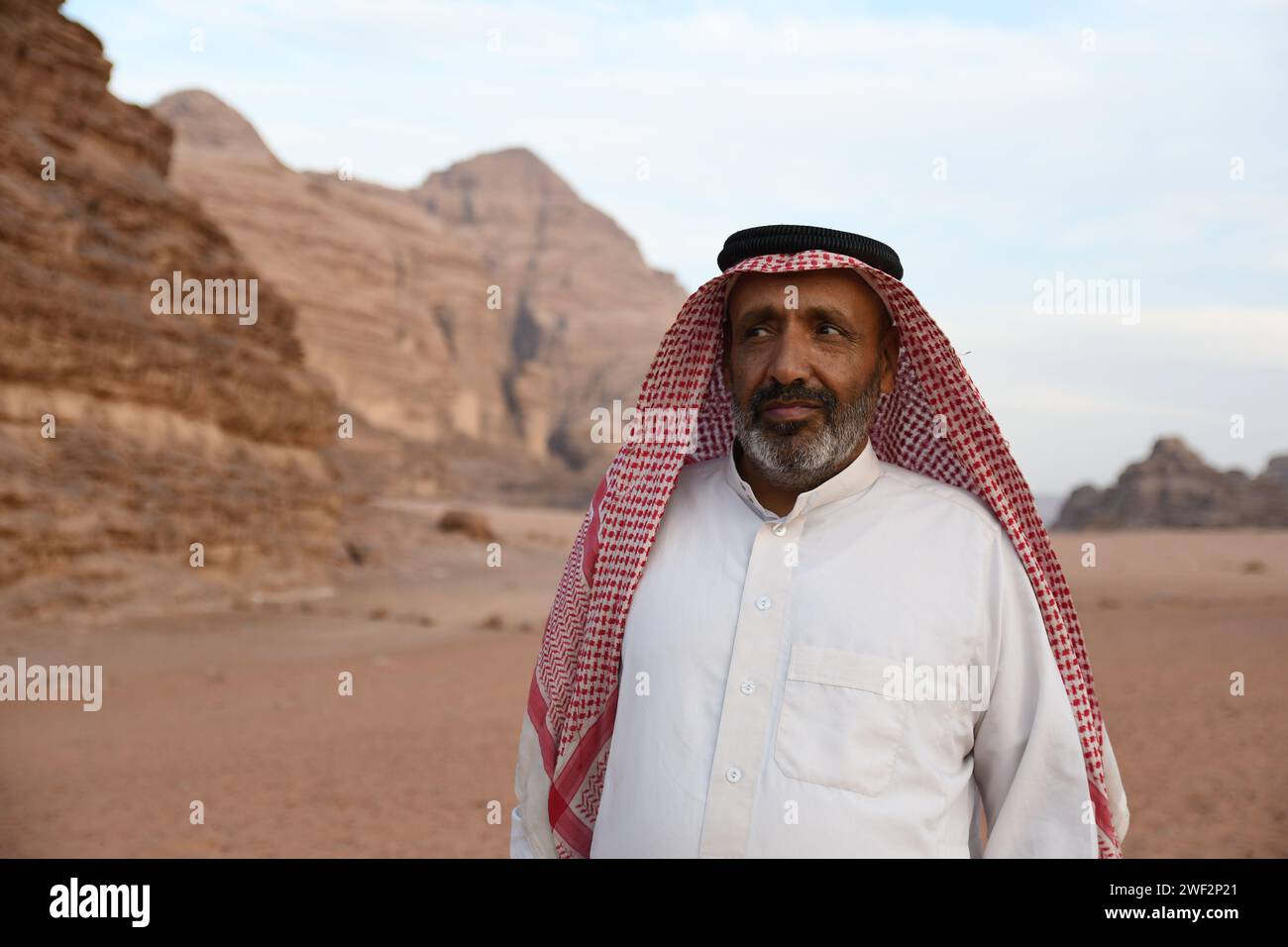 Man in traditional Arab attire standing amidst vast desert rock formations Stock Photo