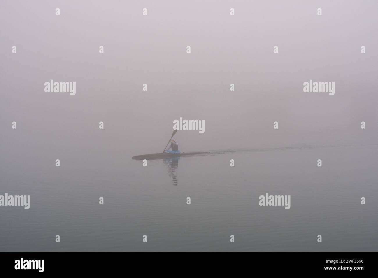 Grado, Italy - January 28th, 2024: Girl practices rowing during a day of thick fog in the sea of Grado. Intense sport with canoe/kayak. Stock Photo
