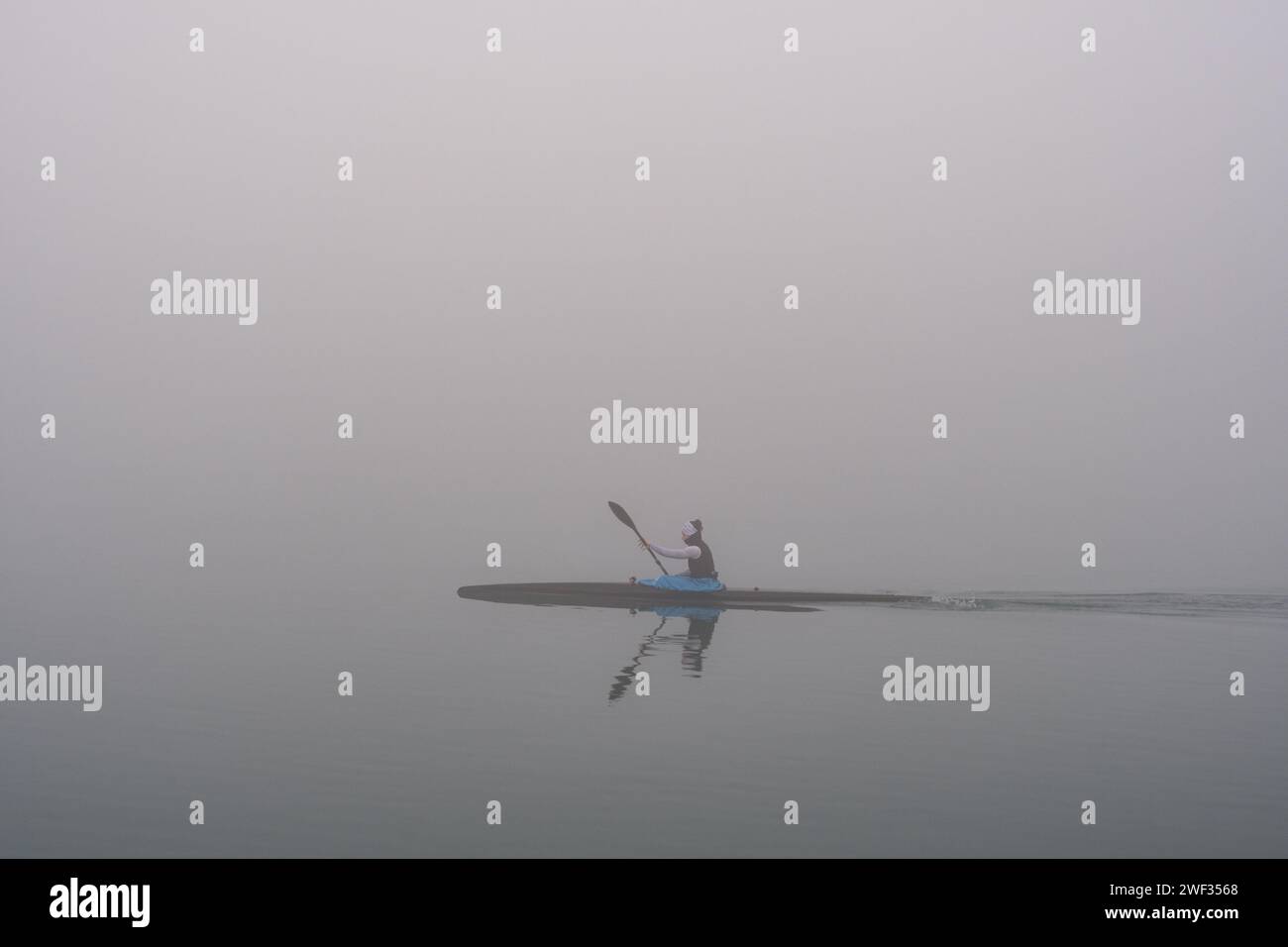Grado, Italy - January 28th, 2024: Girl practices rowing during a day of thick fog in the sea of Grado. Intense sport with canoe/kayak. Stock Photo