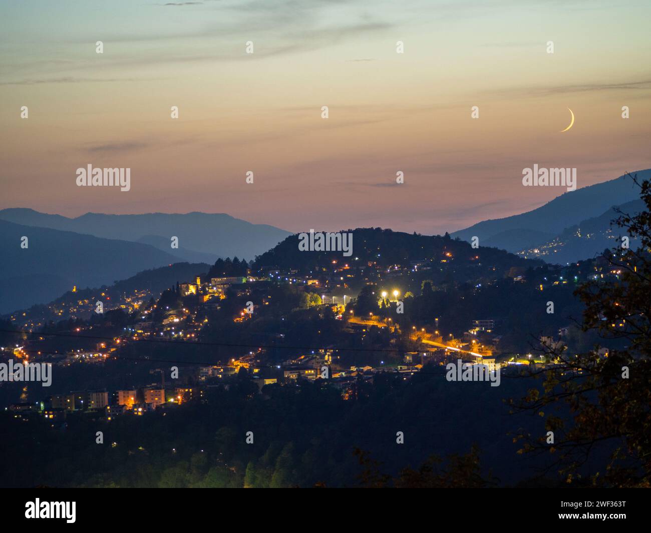 Moon setting over a city behind the mountains Stock Photo