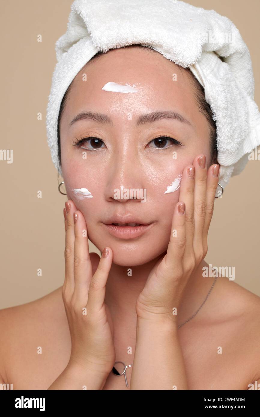 Portrait of young woman applying firming face moisturizer after shower