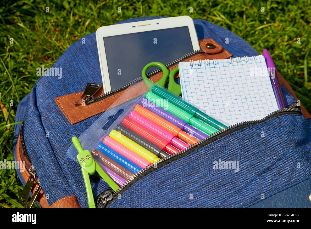 blue backpack with school supplies on the grass Stock Photo
