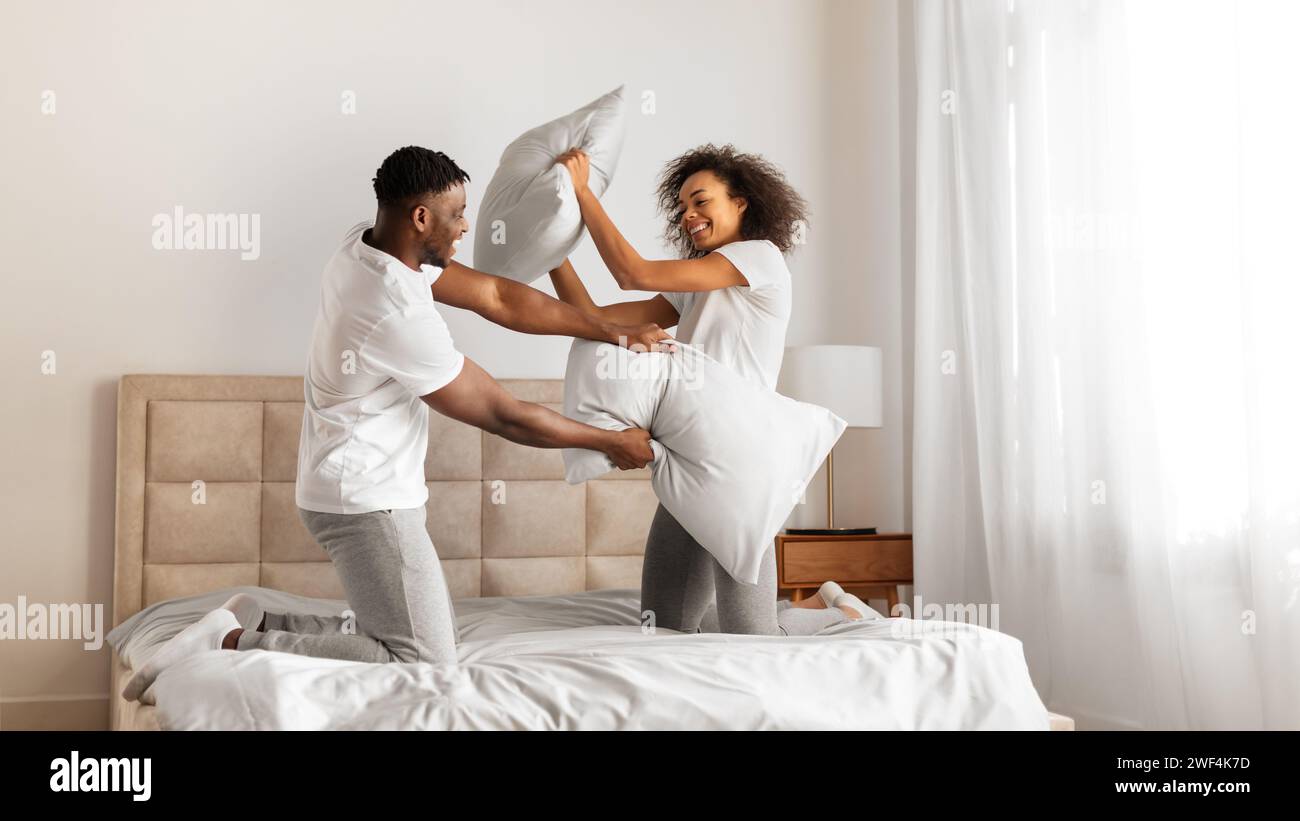 African American spouses having pillow battle for fun at bedroom Stock Photo