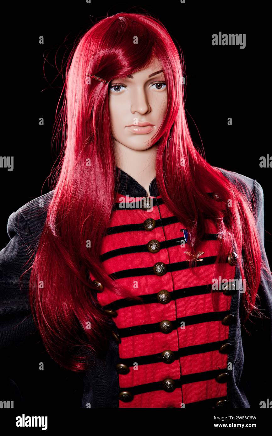 Plastic woman mannequin with soldier coat and red long hair posing for studio shoot on a black background Stock Photo