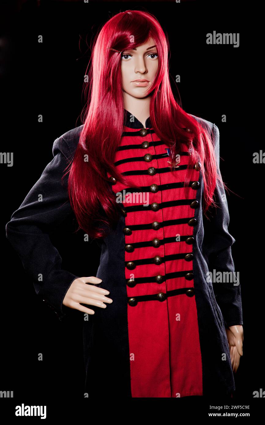 Plastic woman mannequin with soldier coat and red long hair posing for studio shoot on a black background Stock Photo