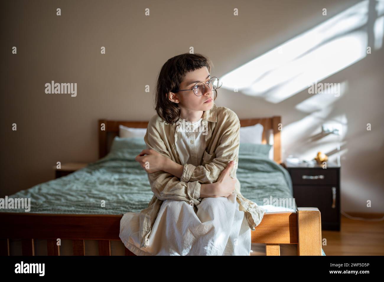 Pensive teen sitting on bed, looking at window, thinking of misunderstanding with friends, parents Stock Photo