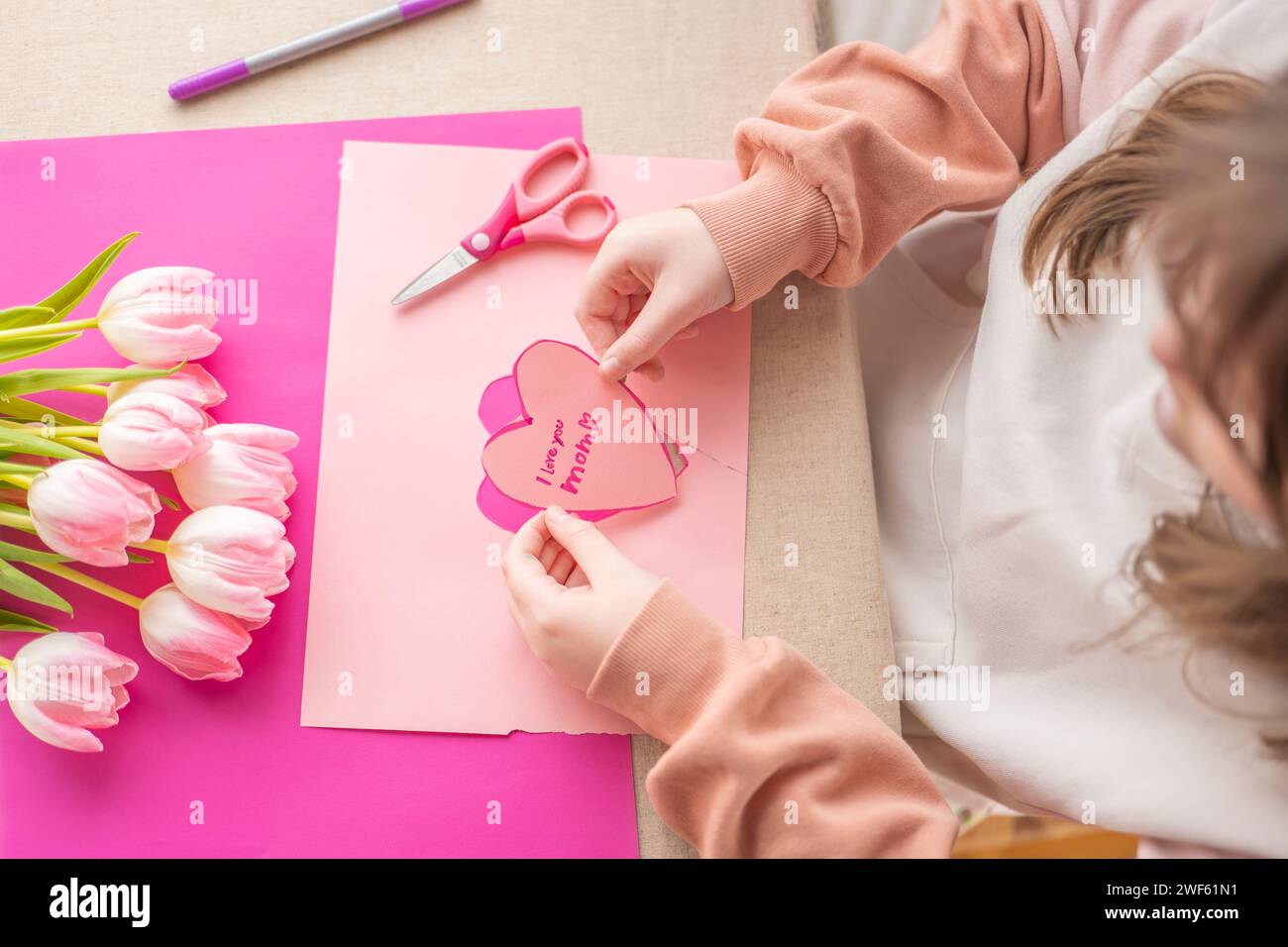 I love you, Mom.moms day concept. Childrens hands holding a heart card.Pink heart card and pink tulips.Flowers and cards for mom. Stock Photo