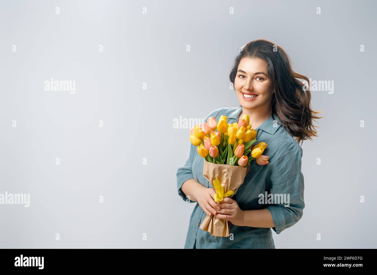 Beautiful young woman with yellow flowers in hands on grey wall background. Stock Photo