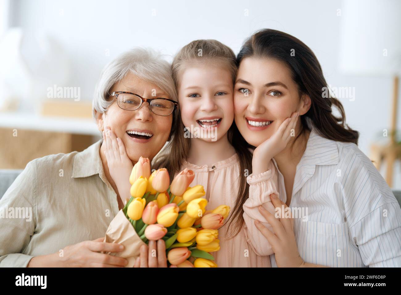 Happy mother's day. Child daughter and mother are congratulating granny giving her flowers tulips. Grandma, mum and girl smiling and hugging. Family h Stock Photo