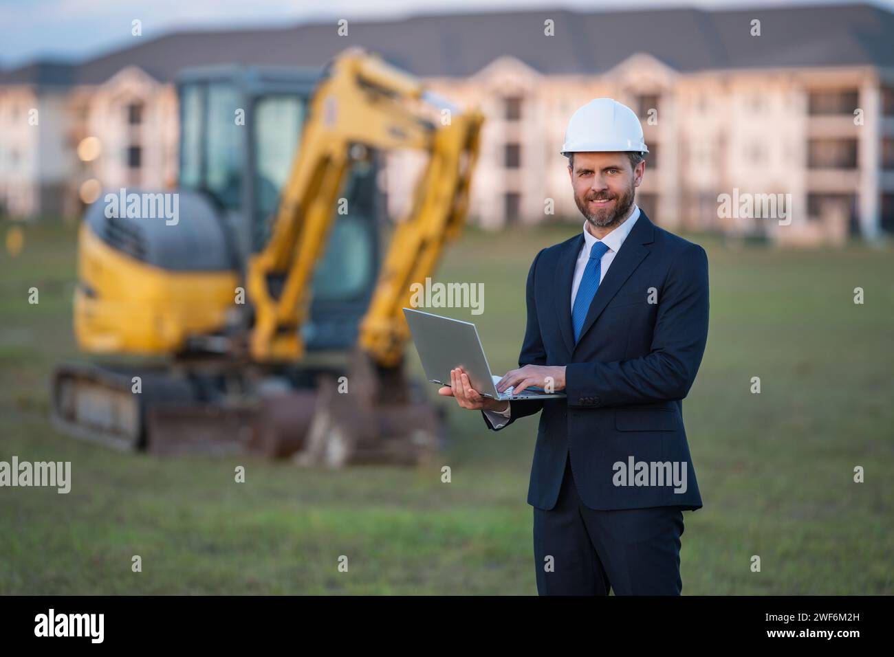 Construction owner near excavator. Confident construction owner in front of house. Architect, civil engineer. Man construction owner with a safety ves Stock Photo