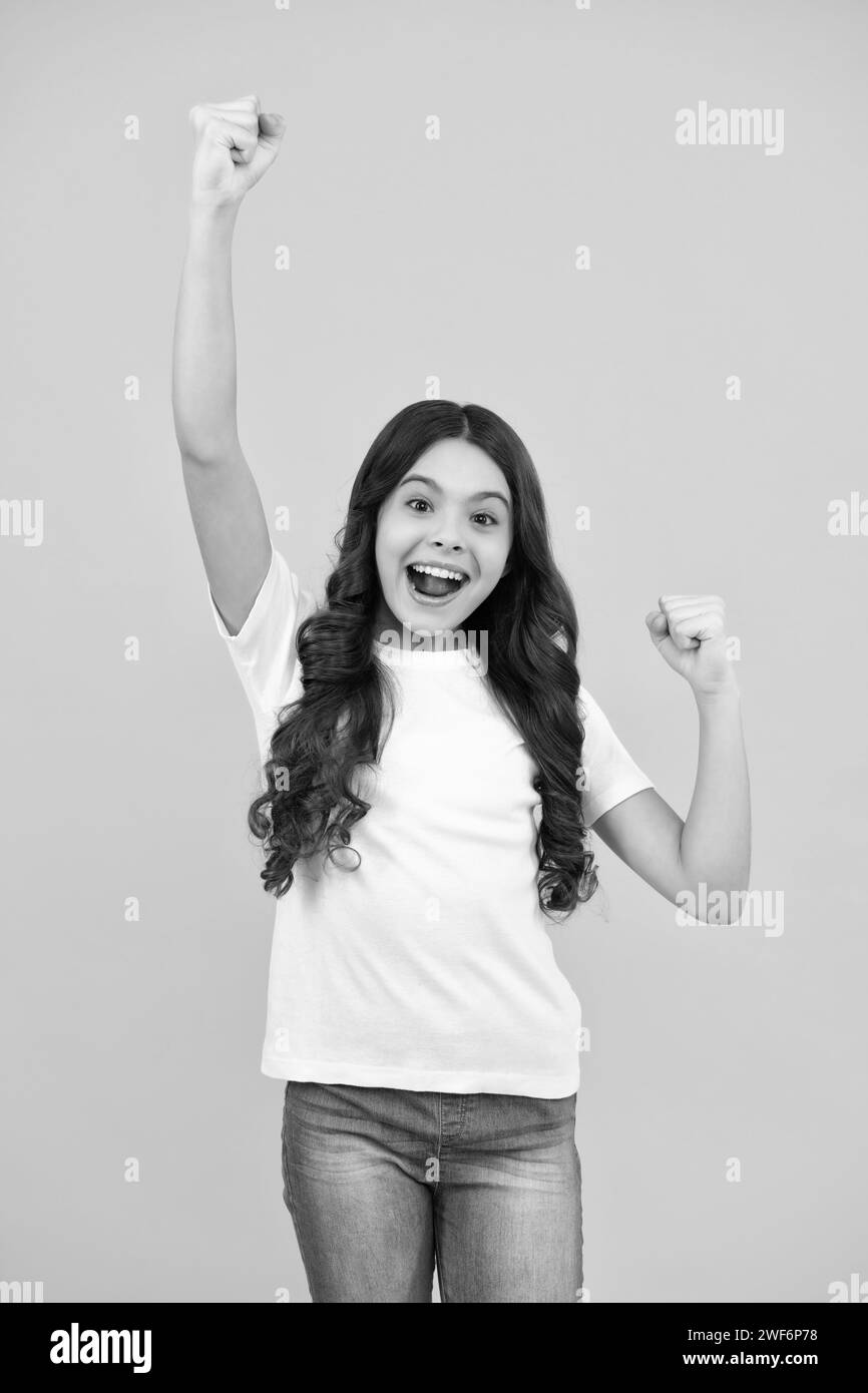 Amazed teenager. Excited teen girl. Teenager child overjoyed successful do winner gesture clench fist say yes isolated on yellow background studio Stock Photo