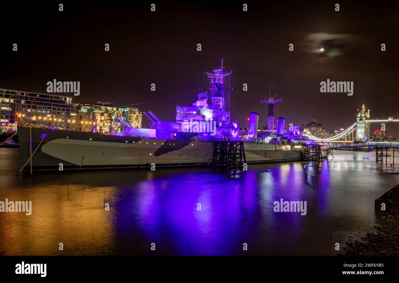 London. UK-01.27.2024. A night view of the entire HMS Belfast battleship museum on the River Thames with Tower Bridge in the background. Stock Photo