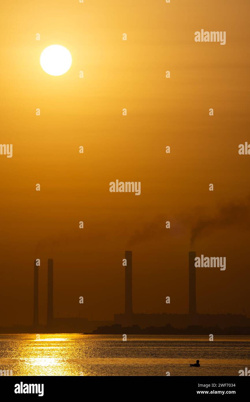The sunset over coastal water with factory chimneys emitting smoke ...