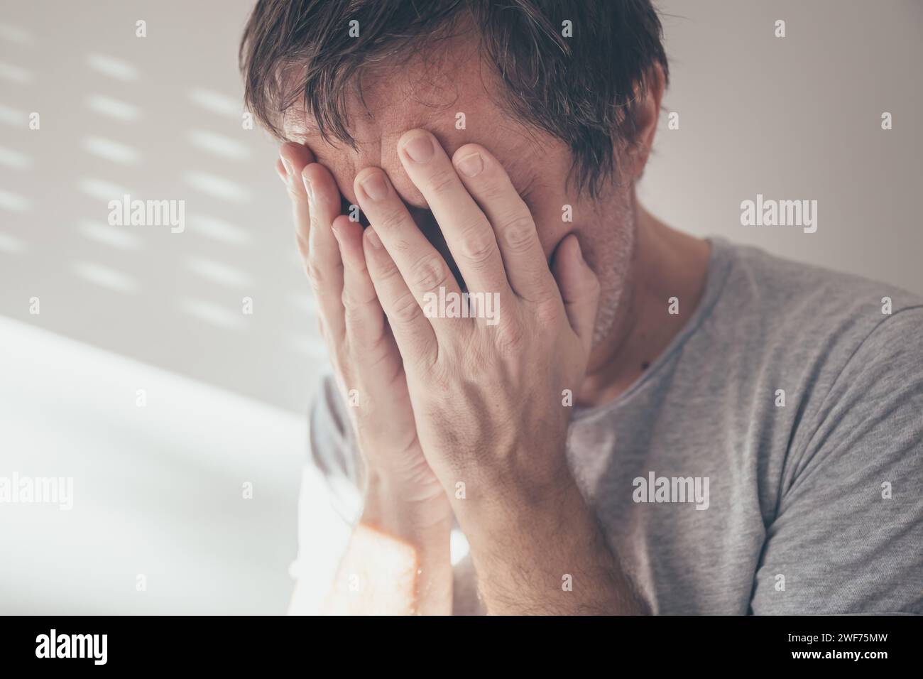 Despair concept, complete loss or absence of hope. Adult caucasian male covering face and crying desperately, selective focus Stock Photo