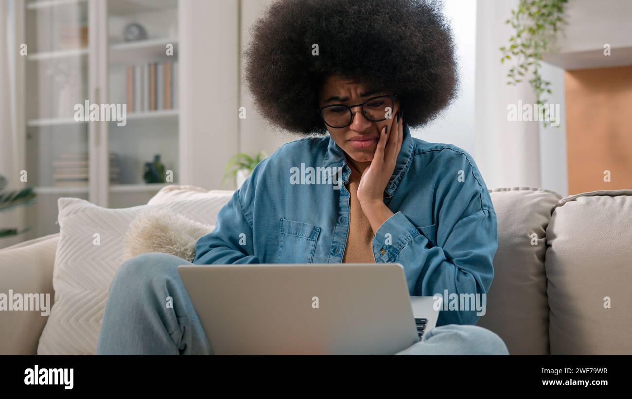 Confused frown African American woman girl reading terrible bad news in laptop at home couch female user freelancer businesswoman using computer shock Stock Photo
