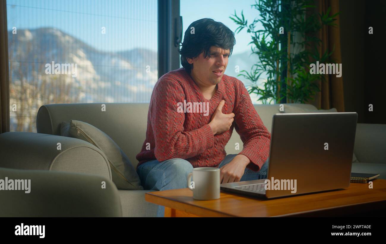 Man sit on sofa suffering chest pain, having heart attack, holding massaging chest while working