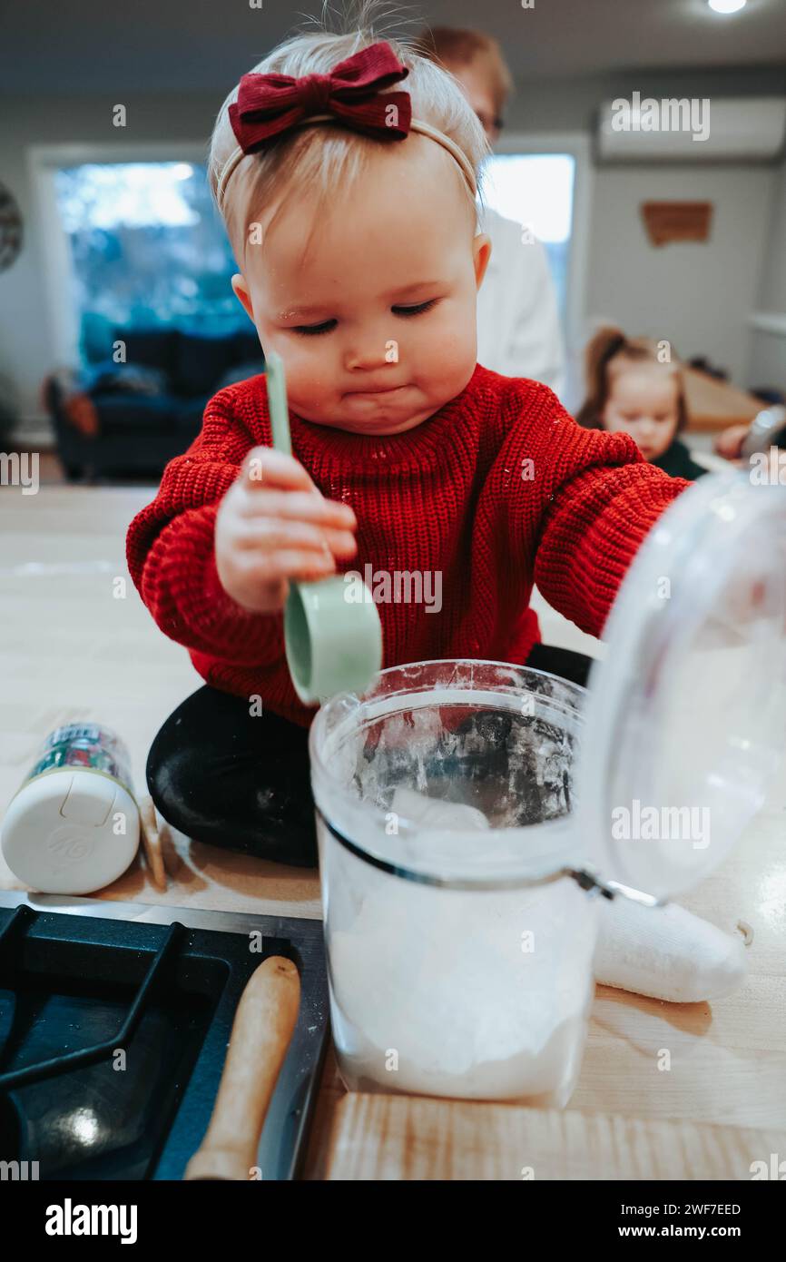 Little girl on counter, scooping flour for baking joy Stock Photo Alamy
