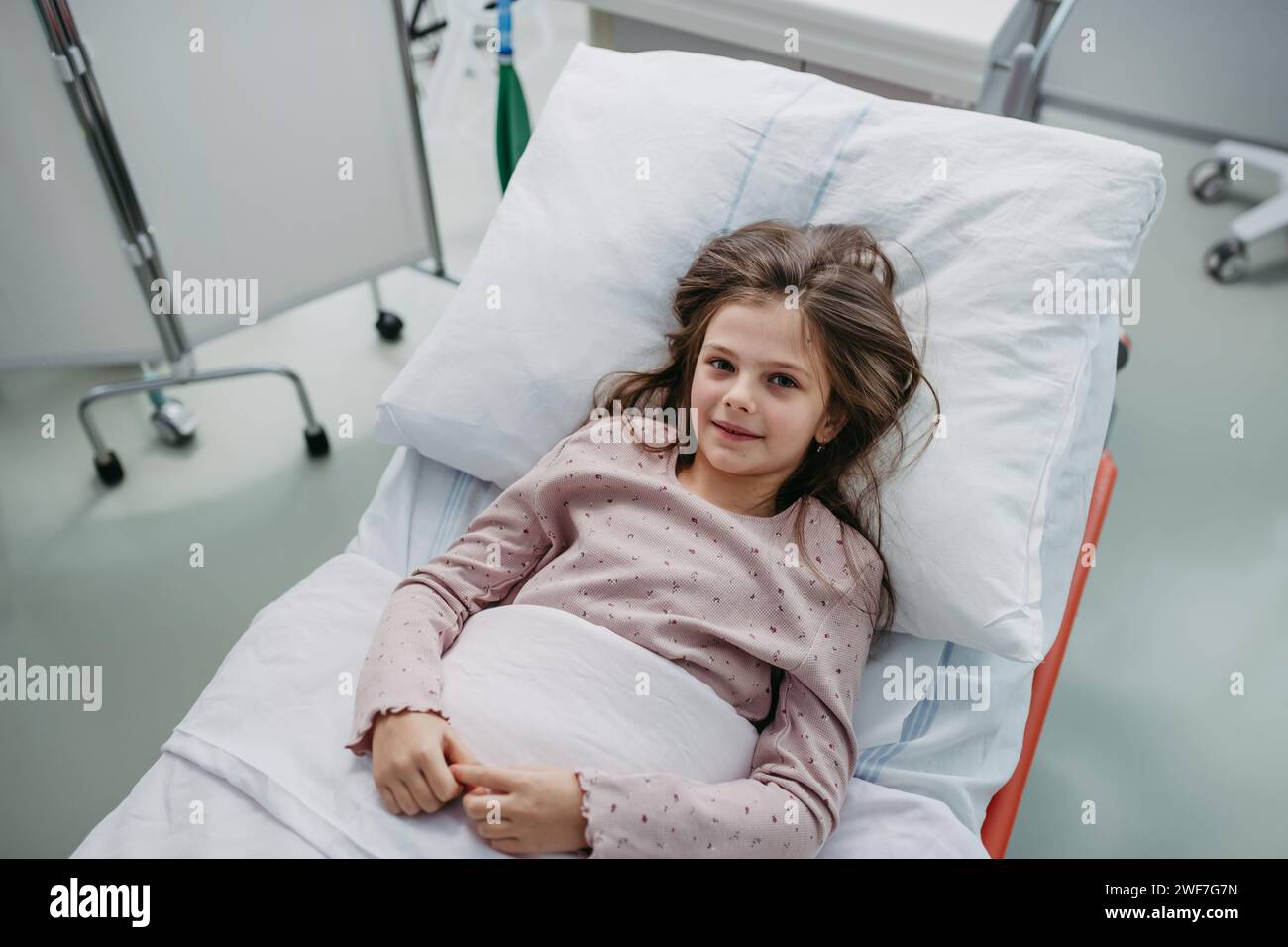Little girl patient lying in hospital bed. Children in intensive care unit in hospital smiling. Stock Photo