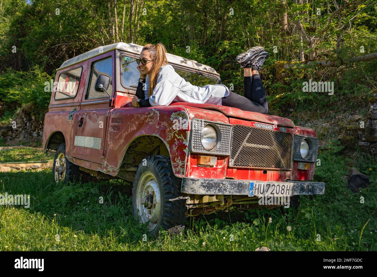 Pensive woman smiles laid on the hood of a vintage red off-road Stock Photo