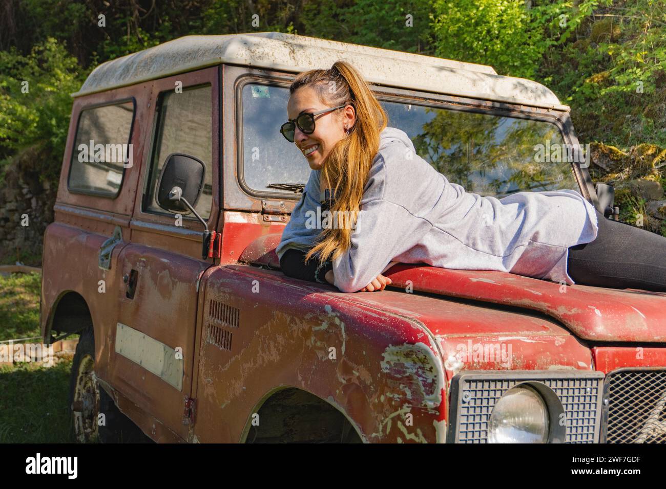 Woman lying on the hood of an old red off-road vehicle parked in Stock Photo