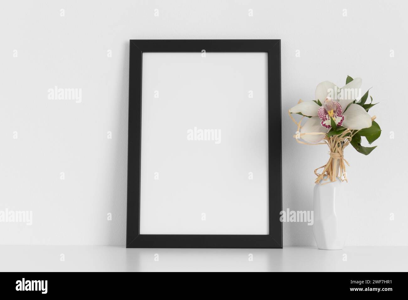 Black frame mockup with a orchid on the white table. Stock Photo