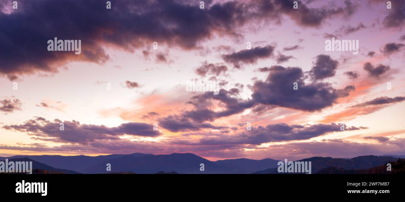 panorama of a dramatic cloudscape at dusk. sky in colorful evening light above the mountain ridge. changing weather forecast Stock Photo