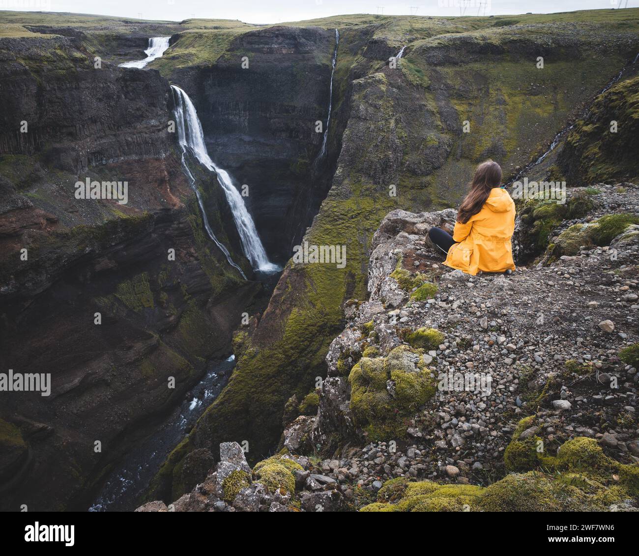 Iceland adventure: yellow rain jacket, rocky outcrop and majestic waterfall Stock Photo
