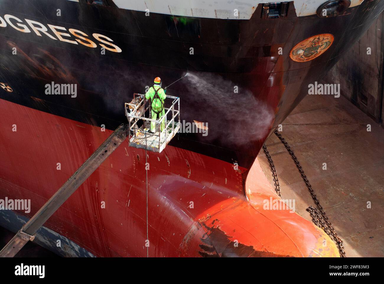 High angle image of a dock worker steam cleaning the hull of a tanker in dry dock. Stock Photo