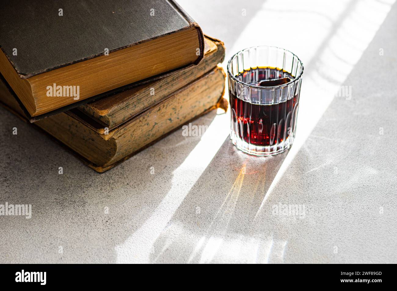 Cherry liqueur in a clear glass beside a stack of vintage books on a sunlit surface Stock Photo