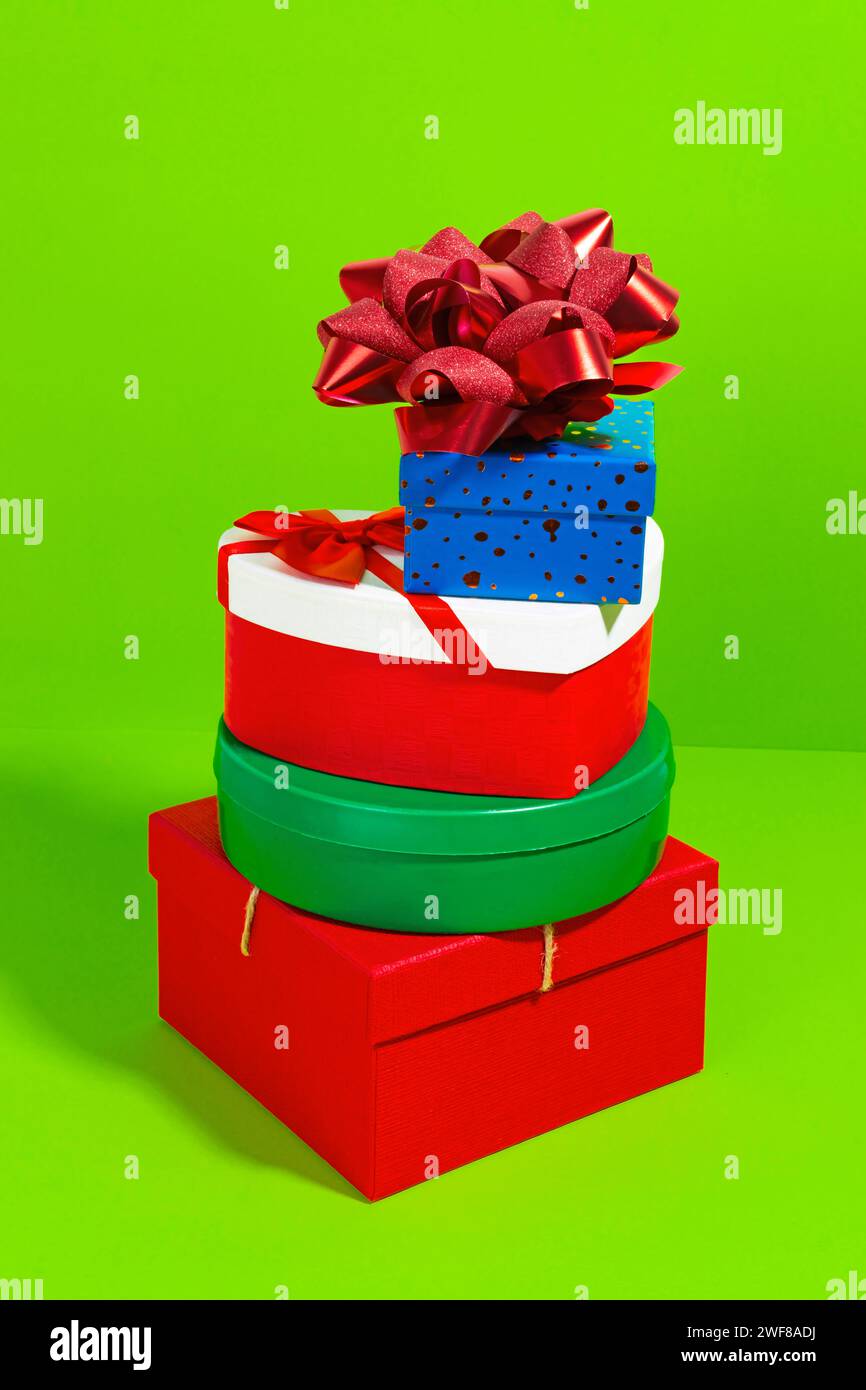 A colorful stack of various shaped gift boxes with a glittering bow on a bright green background Stock Photo