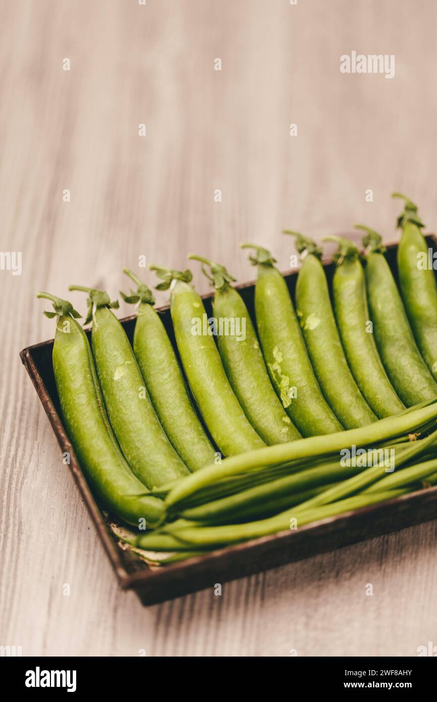 A close-up image showcasing vibrant green peas in a pod neatly arranged in a rustic wooden box, set against a soft wooden background. Stock Photo