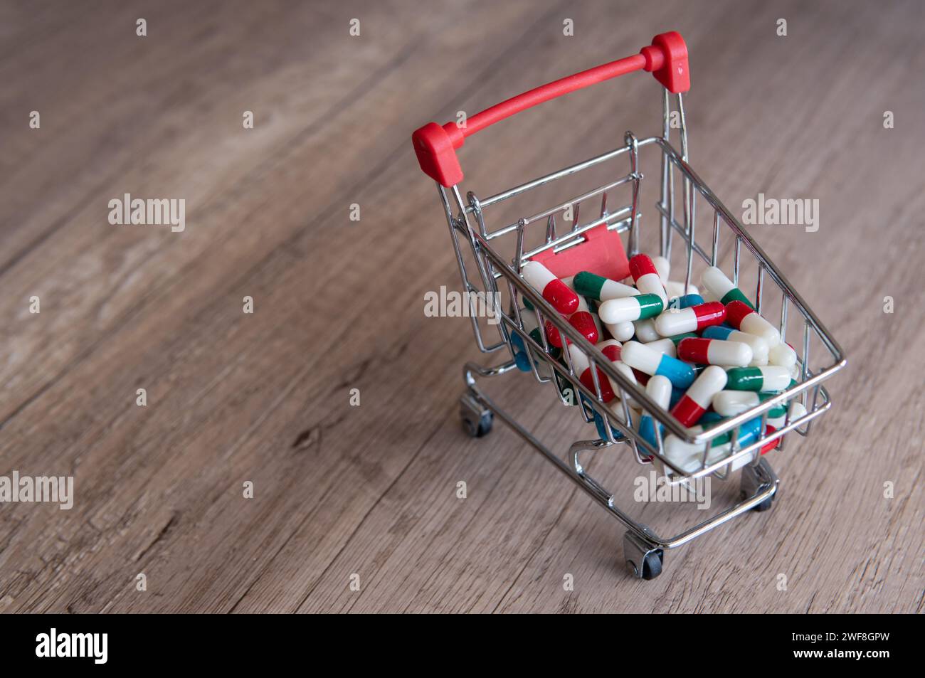 A shopping cart overflowing with colorful pills on a wooden table. Copy space for text. Online pharmacy, healthcare costs concept. Stock Photo