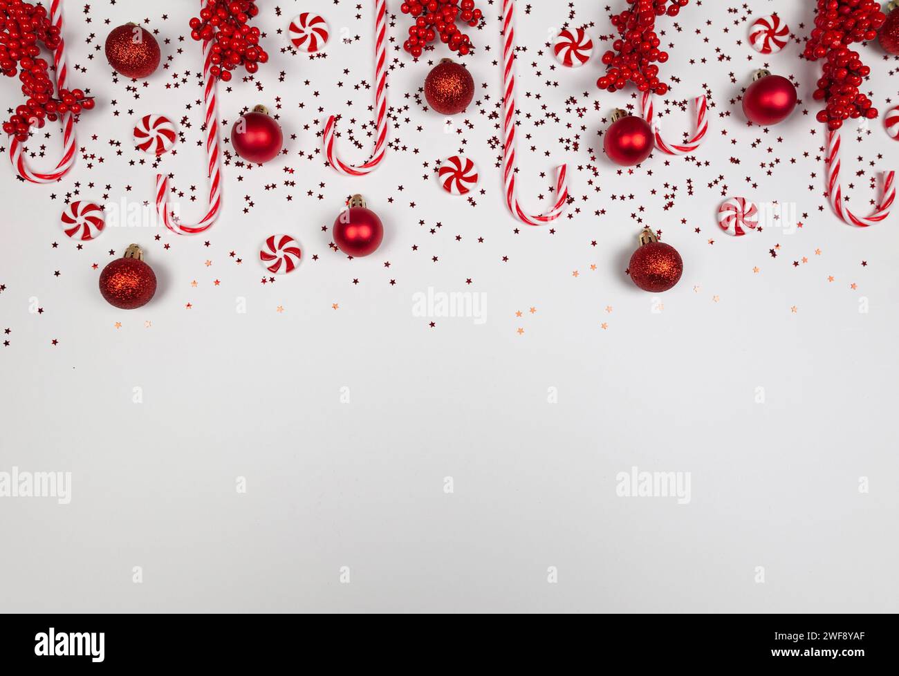 Christmas composition, red and white sweets, red berries, candy canes, red baubles, stars confetti on white background. Stock Photo