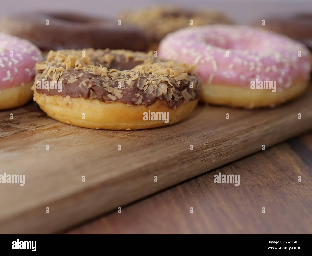 Assorted donuts with various flavors placed on a rustic wooden cutting board Stock Photo