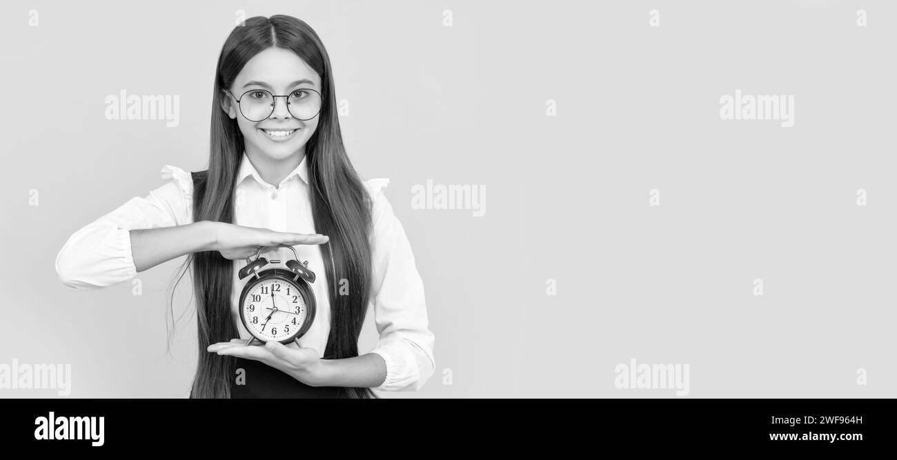 happy kid in school uniform and glasses with alarm clock showing time, school time. Teenager child with clock alarm, horizontal poster. Banner header Stock Photo
