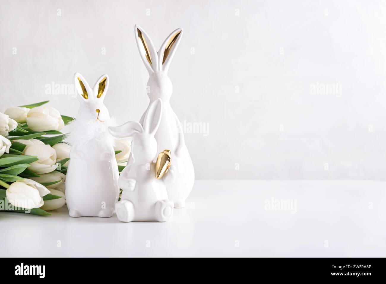 Three Easter rabbits figurines with bouquet of white tulips on white background. Easter celebration concept. Copy space. Front view Stock Photo