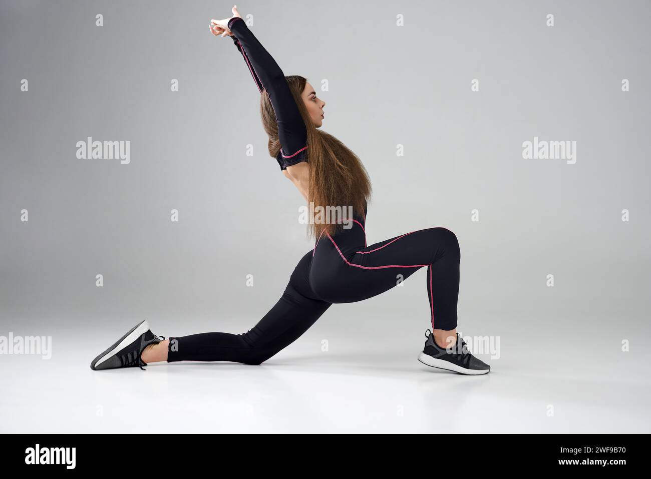 Healthy mind in a healthy body. Flexible cute little girl child looking at  camera while stretching her hands isolated on a grey background. Sport,  training, active lifestyle concept. Horizontal shot. Stock Photo