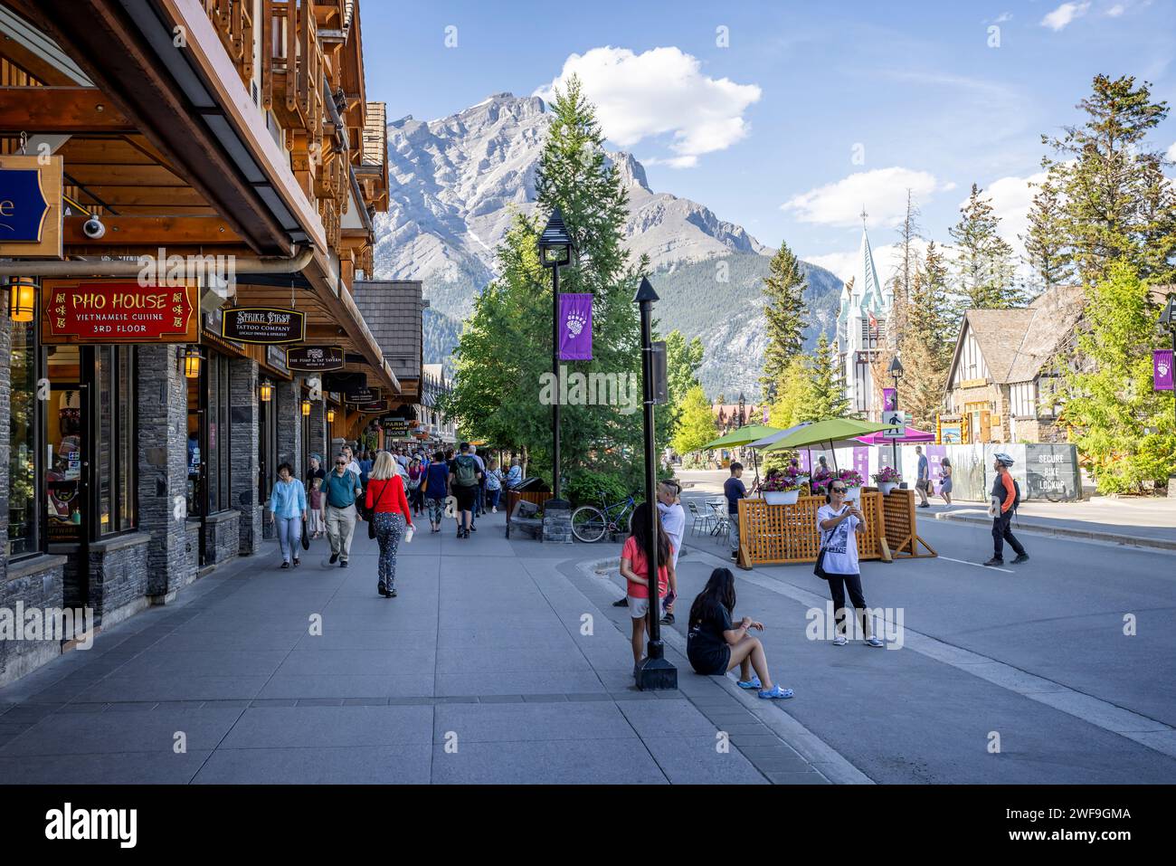 Shops and pedestrians on Banff Avenue with Cascade mountain in the background in Banff, Alberta, Canada on 8 June 2023 Stock Photo