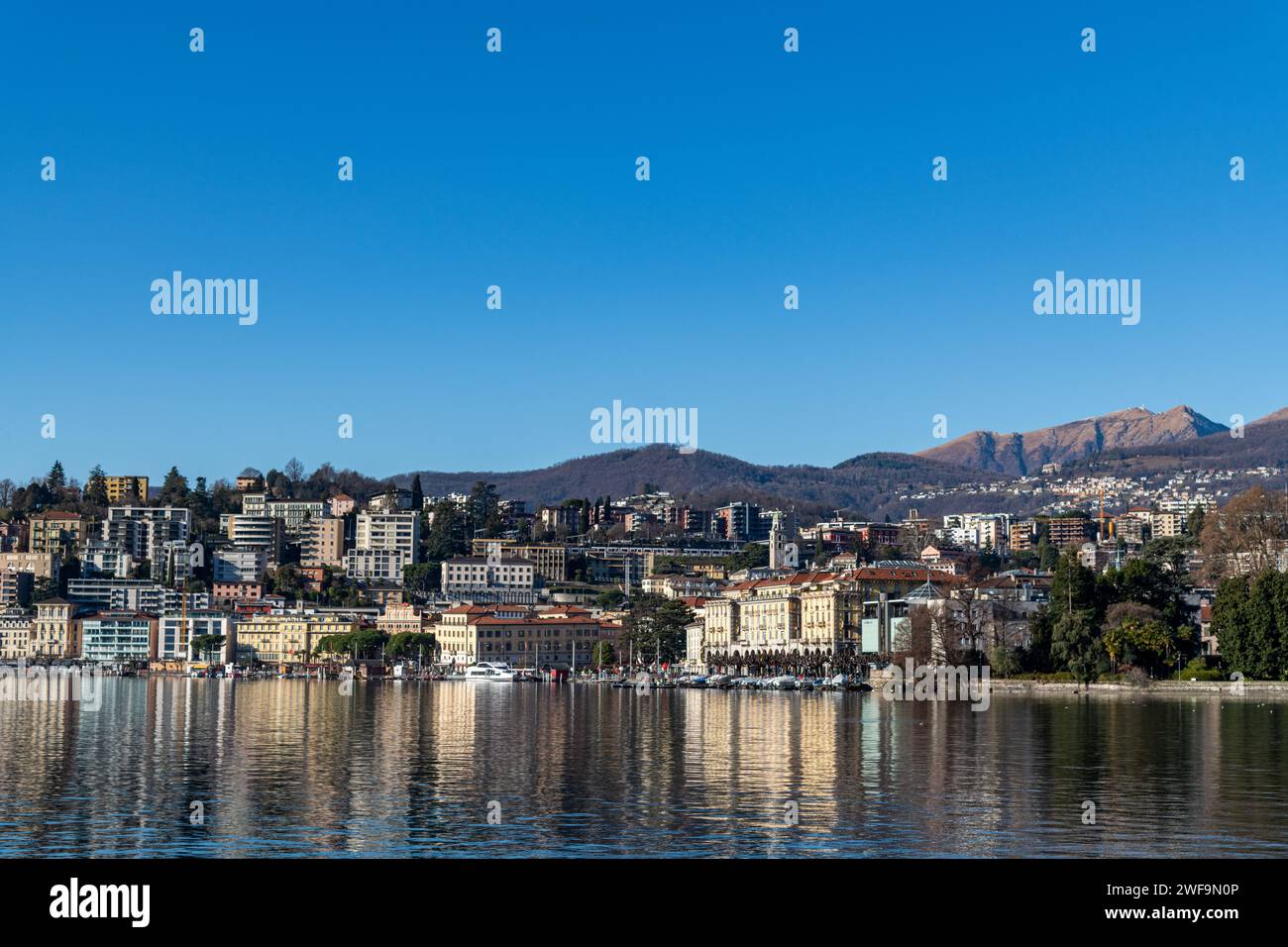 A view of buildings reflected in the water of Lake Lugano in Switzerland Stock Photo