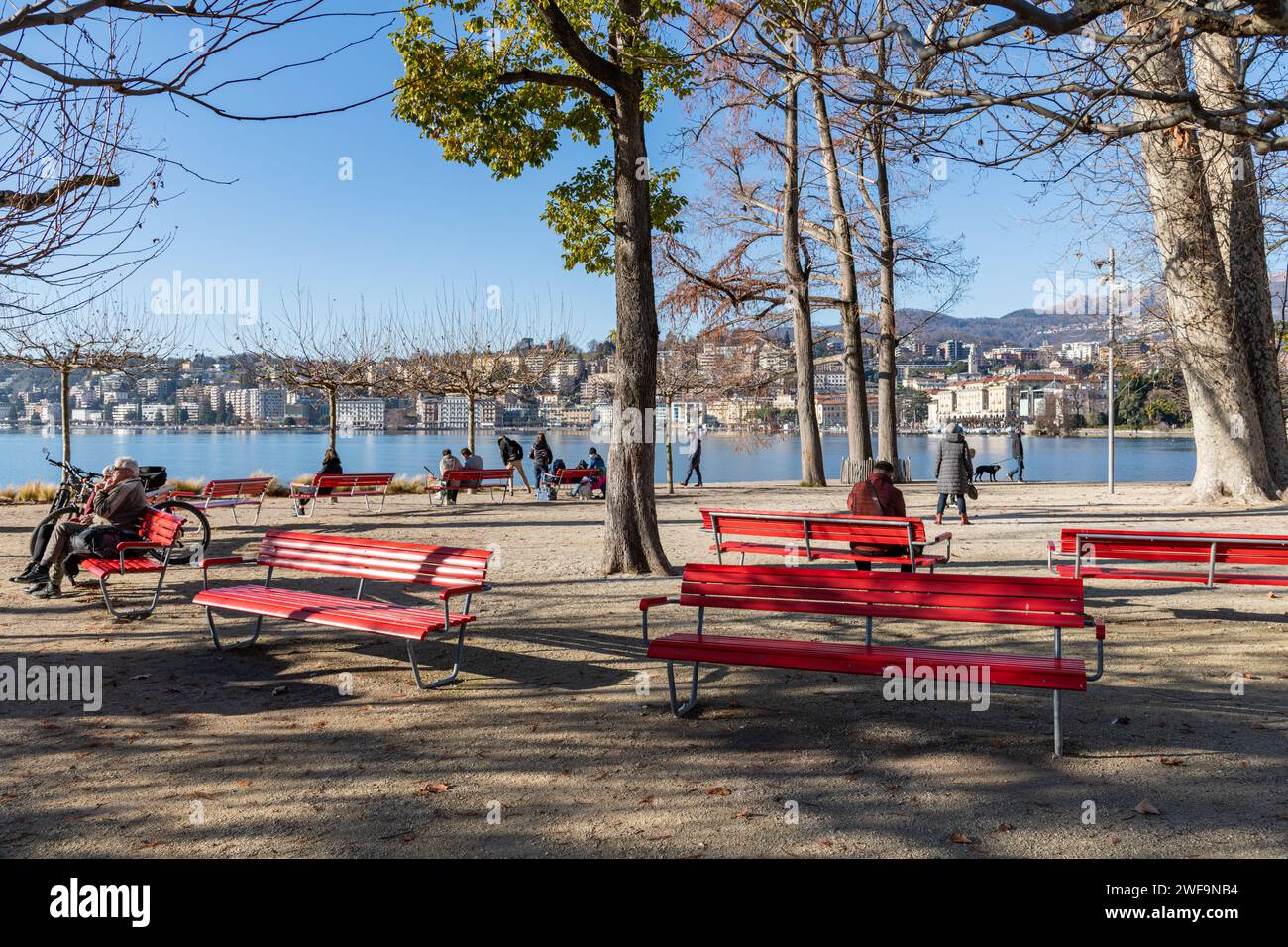 People sat on benches in a park by Lake Lugano in Switzerland Stock Photo