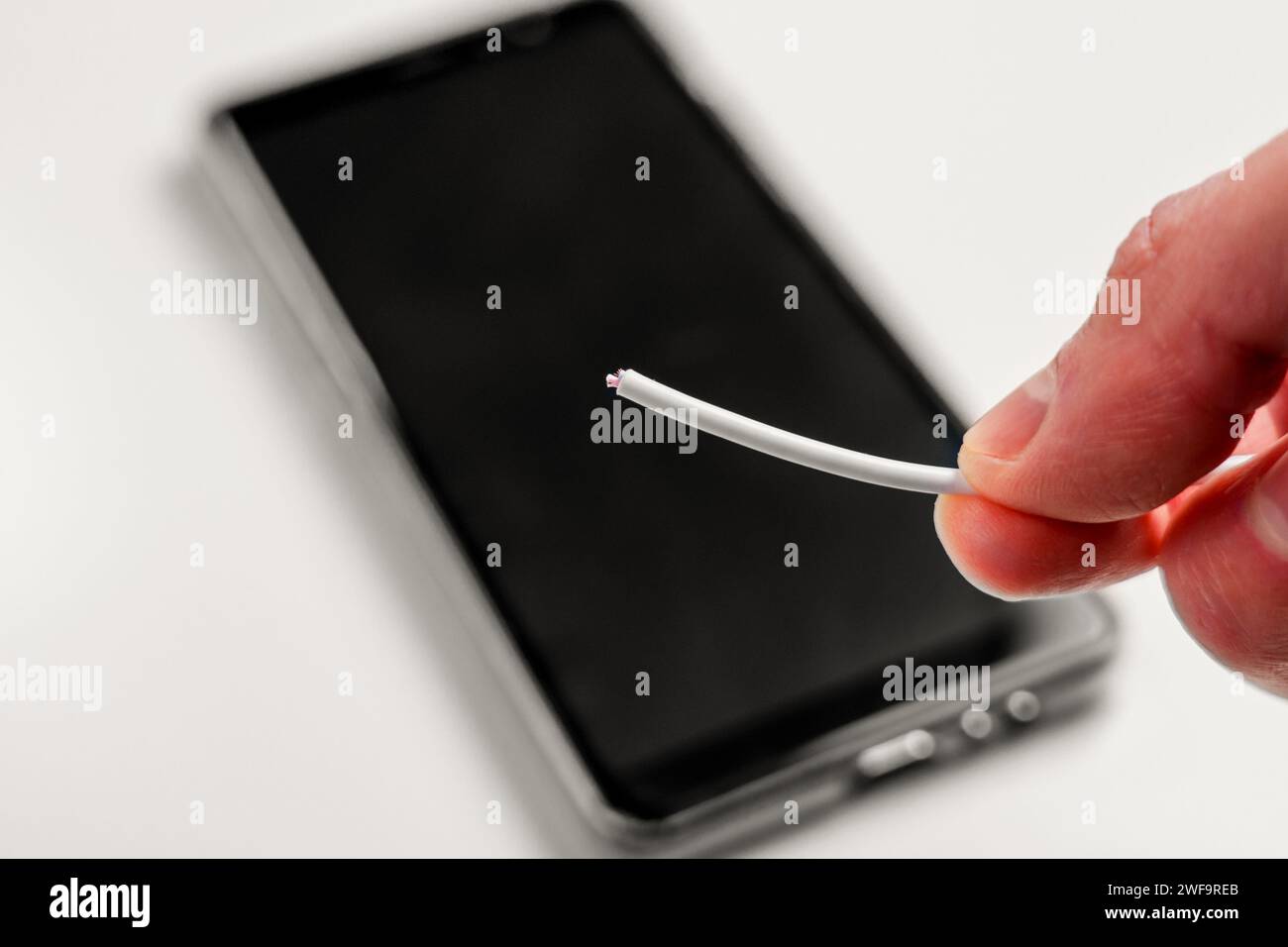 Hand holding a broken torn charger cable with a black smartphone on a